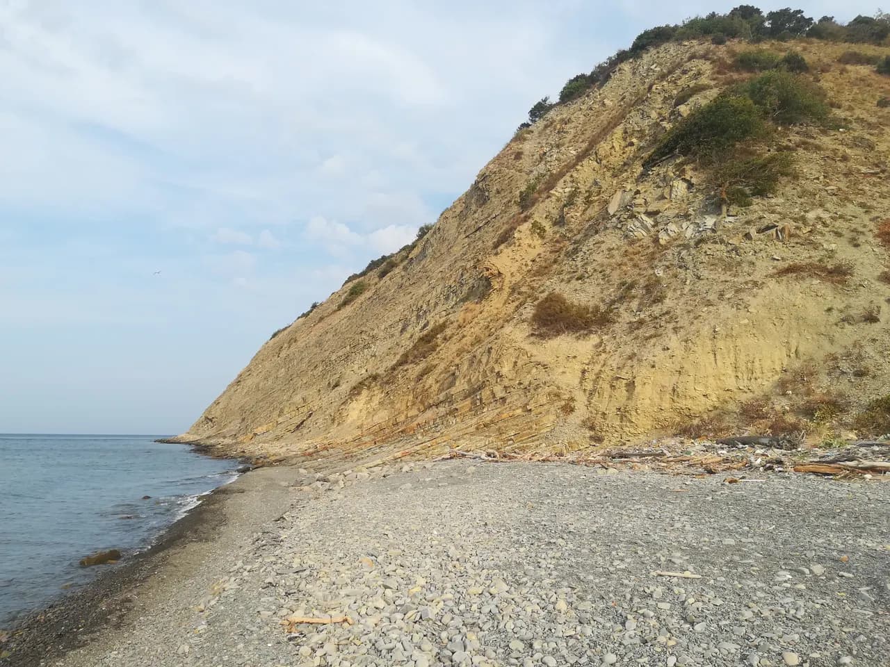 Жёлтый глинистый склон над галечным пляжем Дюрсо, бирюзовая вода у берега